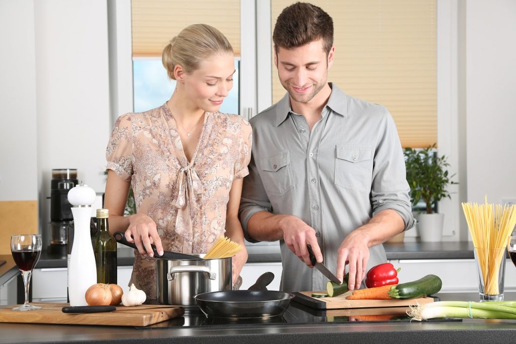 un homme et une femme qui cuisinent ensemble l'homme coupe des légumes et la femme fait cuire des pâtes